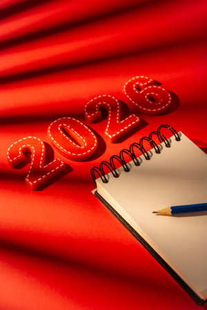 Red numbers 2026, a blank spiral notebook, and a pencil lying on a red background with a palm...