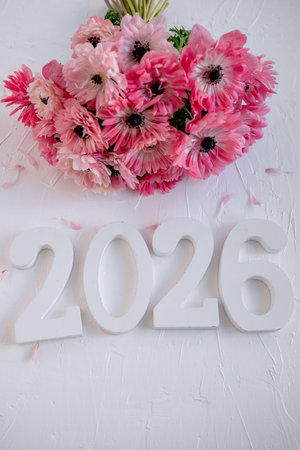 Bouquet of delicate pink anemone flowers and fallen petals arranged with wooden numbers 2026,...