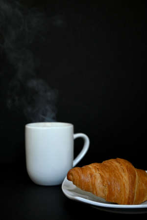 Close-up of delicious homemade golden croissant with cup of hot tea coffee with dark background. Photograph with copy spaceの写真素材