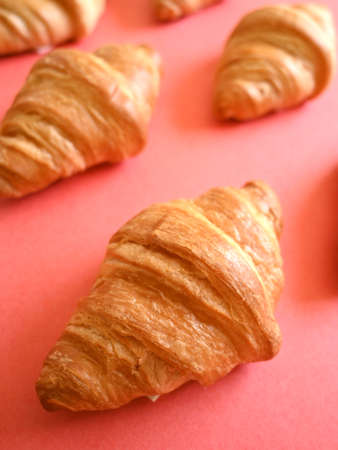 Front shot of pattern of delicious homemade golden croissants on coral backgroundの写真素材