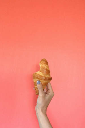 Close-up of latin woman's arm with homemade golden croissant on coral background, with copy spaceの写真素材