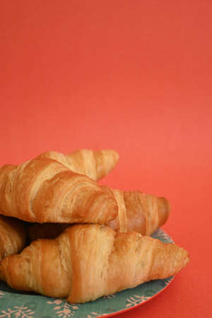 Closeup of delicious homemade golden croissants on turquoise plate on coral background with copy spaceの写真素材