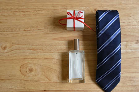 Flatlay of father's day gifts, square white gift box with red bow and tag with "happy father's day" message, blue striped tie, square perfume, on pine wood background with copy spaceの写真素材