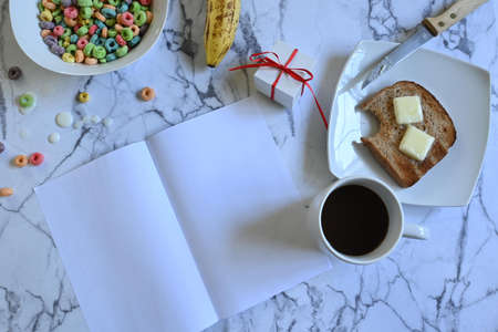 Father's day celebration breakfast, white bowl with colorful cereals and milk, white cup with black coffee and square white plate with toast and butter, small square and white gift with red bow, ripe banana, blank greeting card, marble background, copy spaceの写真素材