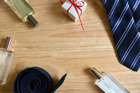 Flatlay of father's day gifts, square white gift box with red bow and tag with "happy father's day" message, blue striped tie, three square perfumes, on pine wood background with copy spaceの写真素材