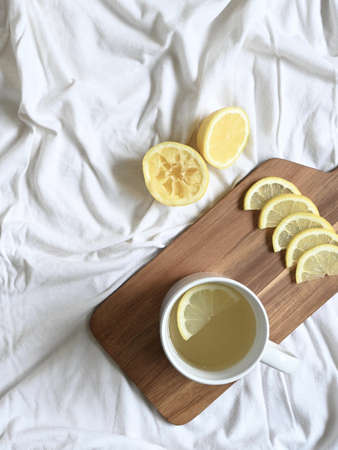 white cup with lemon tea on dark wood table on textured white sheets, with copy spaceの写真素材