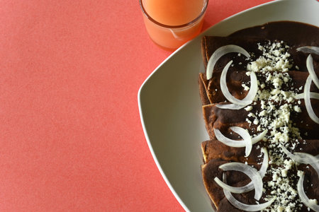 Overhead shot of enfrijoladas with onion and cheese, glass of grapefruit juice, with coral...