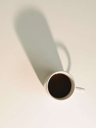 Overhead shot of white cup with coffee with strong shadows, light background and copy spaceの写真素材