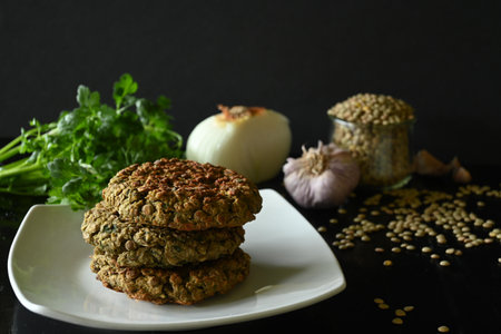 Close-up of lentil burgers next to onion, coriander, garlic, black background and copy spaceの写真素材