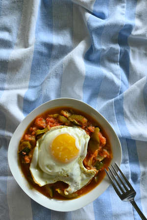 Vertical overhead shot of Manchego pisto dish with egg, blue striped cloth background, with copy spaceの写真素材