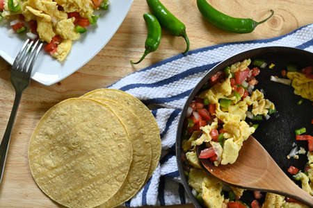 Close-up of Mexican eggs in frying pan, white plate, wooden spoon, wooden table and tortillasの写真素材