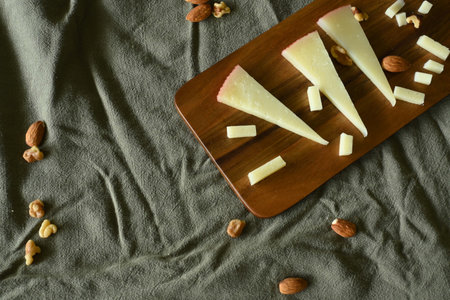 Close-up of manchego cheese with nuts on cutting board, on top of green cloth, with copy space