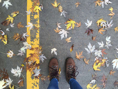 overhead of woman's legs with boots on ground with fallen leaves, autumn conceptの写真素材