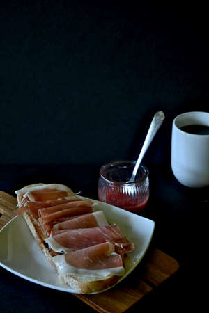 Vertical closeup of cured ham toast with tomato and cup of coffee, black background with copy spaceの写真素材