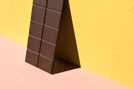 Close-up of chocolate bar with shadows on yellow and pink background, conceptualの写真素材