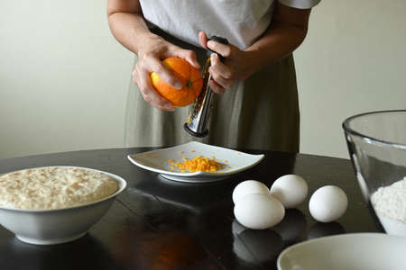 Young woman grating orange surrounded by ingredientsの写真素材