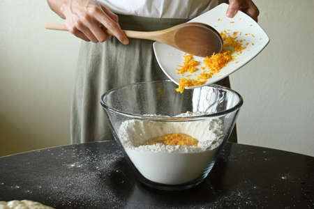Young woman pouring grated orange into dough mixtureの写真素材