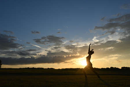 Young woman practicing yoga in the countryside with sunsetの写真素材