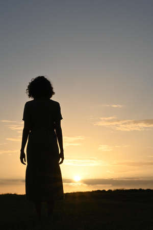 Silhouette of a woman in a dress in front of a sunset.の写真素材