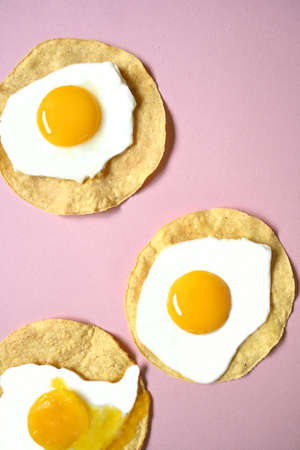 Three fried eggs, one of them broken on a pink backgroundの写真素材