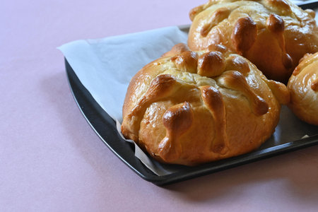 Homemade pan de muerto on a baking sheet, copy space and pink background