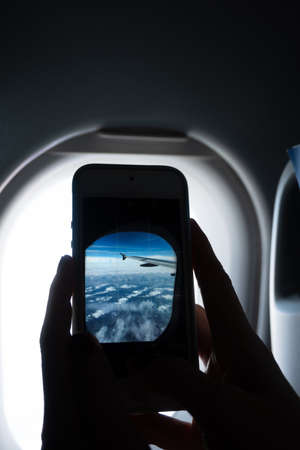 Vertical close-up of hands photographing an airplane window with a cell phone, with copy space.の写真素材