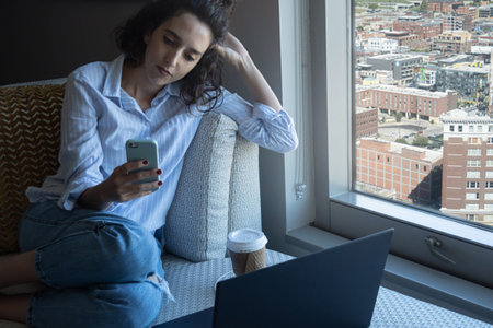 Serious woman looking at smart phone during work break, city views in background, with copy space, home office conceptの写真素材