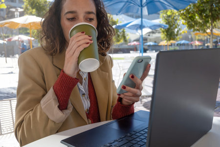 Close-up horizontal close-up latina woman drinking coffee while looking at cell phone and working...