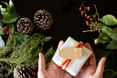 Top view of hands holding gift with empty tag, Christmas decoration, black background and copy space.の写真素材