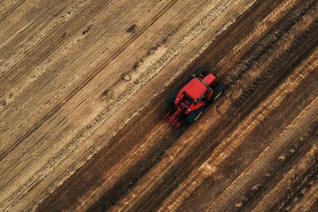 Red tractor is plowing a field, creating perfectly straight rows of fertile soilの素材
