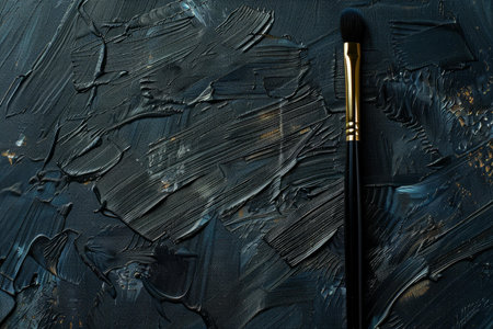 Makeup brush is laying on a textured black and gold painted backgroundの素材
