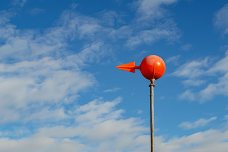 Orange windsock showing wind direction blowing against a bright blue skyの素材