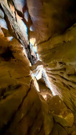 Vertical Cave Passage with Sunlight Illuminating Golden Rock Wallsの写真素材
