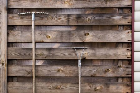 rake and chopper hanging on a wooden wall from old textured boardsの写真素材