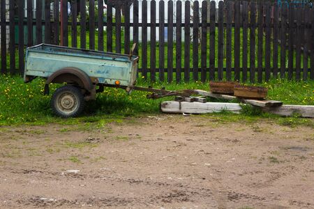 an old blue trailer stands in a village, old rusty wheel rims hold itの写真素材