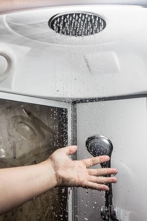 the hand checks the water temperature. Water flows from the shower headの写真素材