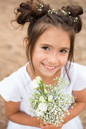 a child girl holds a bouquet of white flowers on a blurry background.dark hair , white flowers in her hands, white dressの写真素材