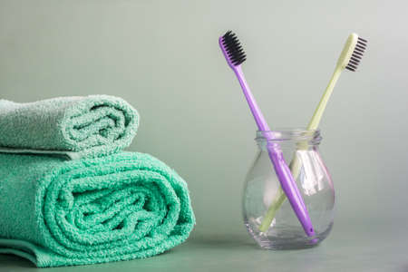 two toothbrushes in a glass jar and two aquamarine towels on a gray backgroundの写真素材
