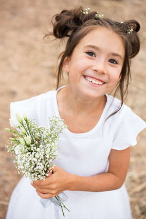 a child girl holds a bouquet of white flowers on a blurry background.dark hair , white flowers in her hands, white dressの写真素材