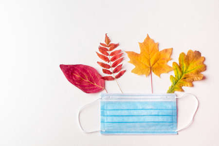 protective mask lies on autumn leaves on a white background. Symbol of the second wave of coronavirus in autumnの写真素材