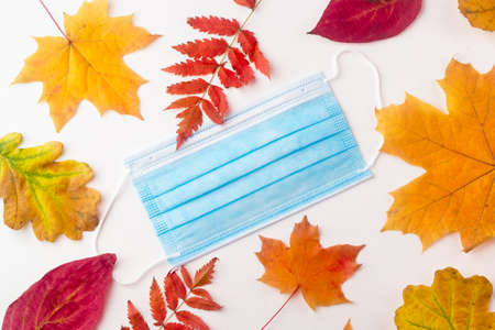 protective mask lies on autumn leaves on a white background. Symbol of the second wave of coronavirus in autumnの写真素材