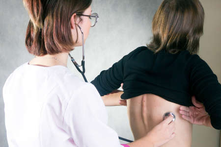 a young female doctor listens to a patients lungs through a phonendoscopeの写真素材