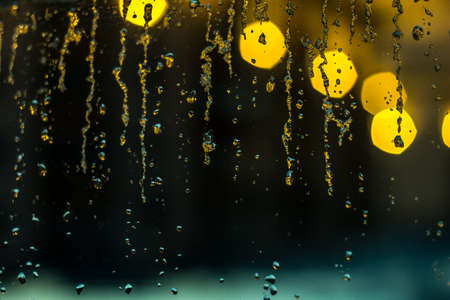 abstract background, streams of rain and snow on the glass on the background of street lightingの写真素材