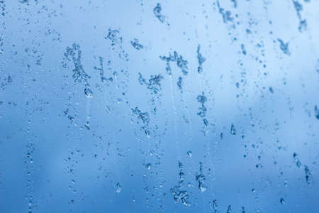 abstract background, streams of rain and snow on the glass on the background against the blue of a stormy skyの写真素材