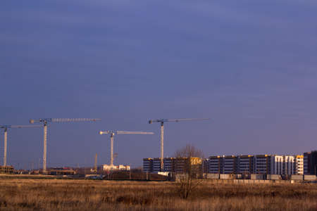 construction site with tower cranes in a field against a dark blue skyの写真素材