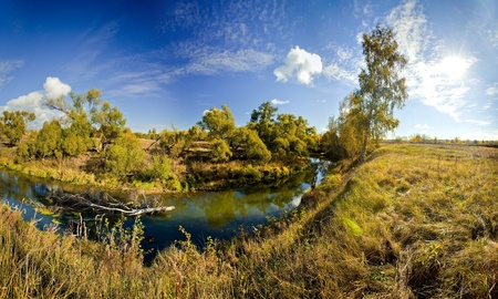 Panoramic landscape of sunny autumn field with forest riverの写真素材