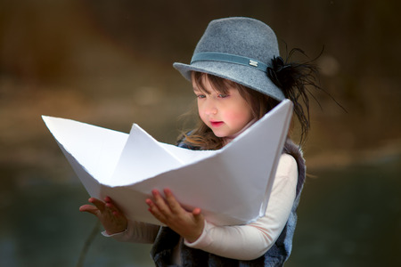 Girl with big paper boat near river at spring cloudy dayの写真素材