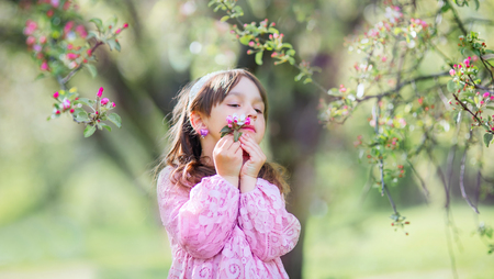 Little happy girl  under blooming crabapple tree with pink flowersの写真素材