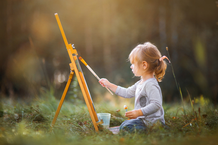Little girl painting at easel in autumn parkの写真素材