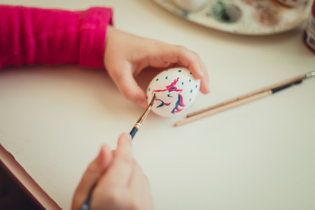 Girl painting on the easter egg at the desk at daylightの写真素材